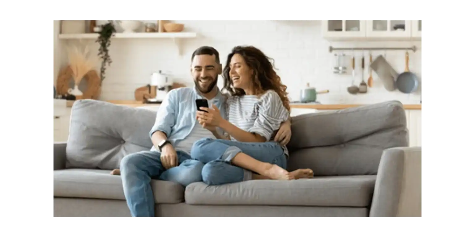 two happy people sitting on the sofa and showing each other something on their phones' screens