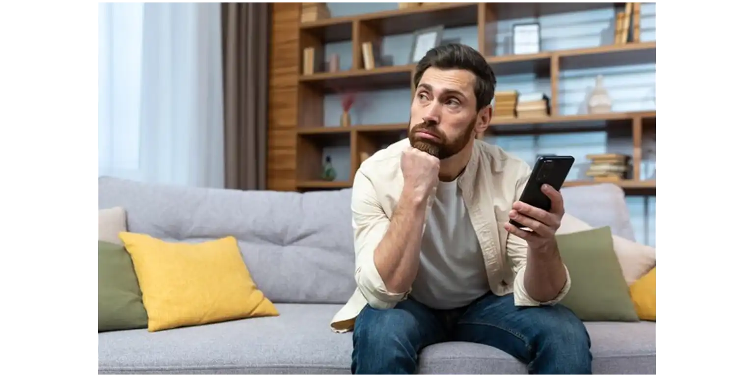 a sad man sitting on a sofa with a turned off phone near him